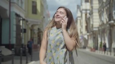 Şehir Sokağı üzerinden yürüyen cep telefonu ile konuşan sevimli genç kadın. Eğlenceli kız açık havada zevk şık yaz elbisesi giyiyor. Yavaş hareket.