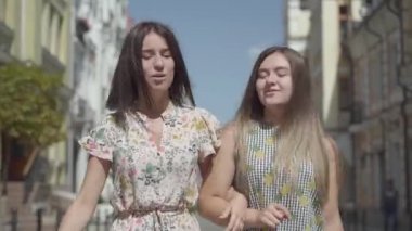 İki neşeli kadın alışveriş poşetleri ile şehir sokakta yürüyüş. Birlikte vakit geçirmek zevk şık yaz elbiseleri giyen genç kızlar. Alışveriş yaşam tarzı konsepti.