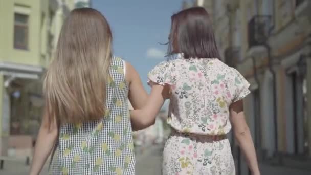 Vue arrière de deux femmes marchant avec des sacs à provisions. Les jeunes filles portant des robes d'été élégantes profiter de passer du temps. Concept de style de vie shopping. Mouvement lent . — Video