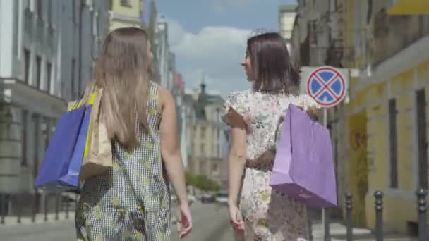 Вид ззаду на двох ходячих жінок з сумками. Молоді дівчата в стильних літніх сукнях насолоджуються проведенням часу. Концепція способу життя в магазинах . — стокове відео