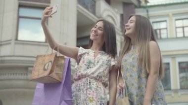 İki mutlu kız alışveriş poşetleri cep açık havada selfie alan alışveriş sonra. Mutlu kızların boş olması. Şehir sokakta yürürken Carefree bayanlar.