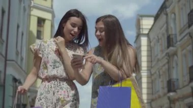 İki mutlu kız cep telefonu ekranına bakarak haber tartışmak güzel binalar önünde alışveriş çantaları ile alışveriş sonra. Pozitif Fashionista kızların boş