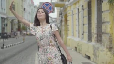 Carefree genç kadın eski bir Avrupa kentinin sokakta taksi yakalamak için çalışırken ellerde alışveriş torbaları ile yaz elbise giyiyor. Mutlu kız boş. Alışveriş zamanı, tatil