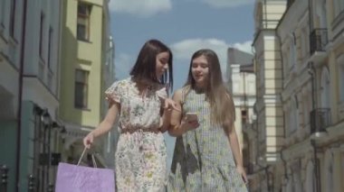 İki sevimli kız cep telefonu ekranına bakarak haber tartışmak güzel binalar önünde alışveriş torbaları ile alışveriş yaptıktan sonra. Pozitif Fashionista kızların boş
