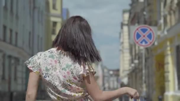 Mujer joven despreocupada con bolsas de compras en las manos caminando por la vieja ciudad europea, bailando y dando vueltas, escuchando música en auriculares. Ocio de chica feliz — Vídeo de stock