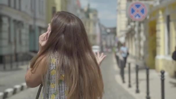 Uma jovem confiante a andar pela velha cidade europeia, a falar ao telefone, a acenar com os braços. Lazer de menina feliz. Visão traseira — Vídeo de Stock