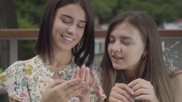 Dos chicas guapas sentadas al aire libre charlando sobre una nueva manicura, mostrando los dedos y las uñas. Las novias hablan de asuntos cotidianos. Tiempo libre de verano — Vídeos de Stock