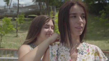 Kız arkadaşları boyun yakın-up etrafında gümüş zincir koyarak. İki çekici kız ışık elbiseler birlikte şehir parkında. Arkadaşına hediye veren bir öğrenci. Summertime Leisure