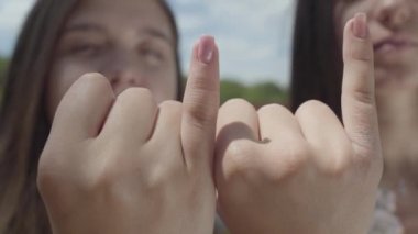 Yakın çekim çekici kızların birbirlerinin küçük parmaklar ve gülümseyen, mavi gökyüzü önünde kamera bakarak alarak. Uzlaşma jest, dostluk kavramı. Summertime Leisure.