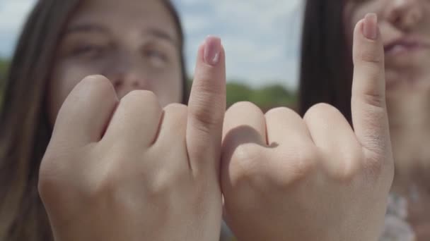 Close-up of attractive girls taking each others little fingers and smiling, looking in the camera in front of blue sky. Conciliatory gesture, friendship concept. Summertime leisure. — Stock Video