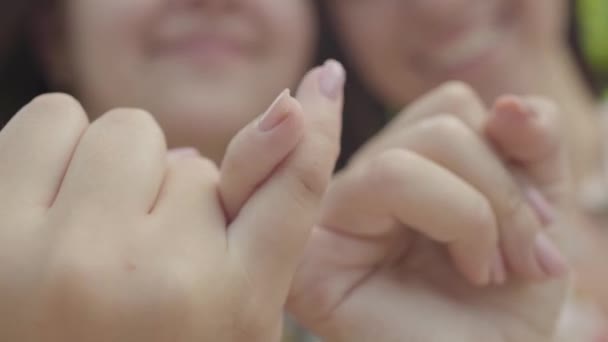 カメラの前で、お互いに小指を取り合い、微笑む女の子の手のクローズアップ。調停ジェスチャー、友情の概念。サマータイムレジャー. — ストック動画
