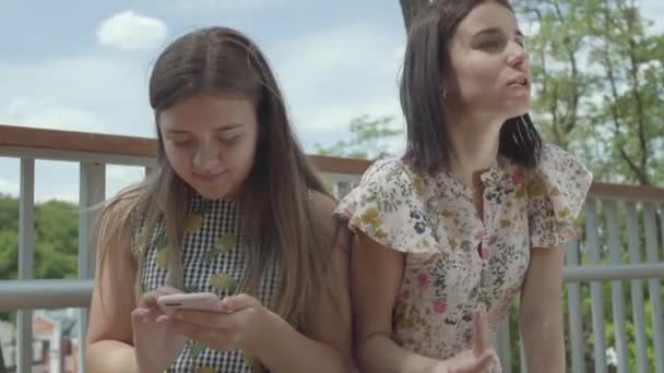 Eine emotionale junge Frau, die ihrem Freund ihre Geschichte erzählt, aber nicht zuhört, indem sie auf dem Handy im Freien sitzt. süße Studentin teilt das Problem mit ihrem Freund, gestikuliert aktiv — Stockvideo