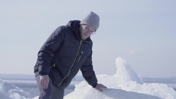 年轻的胡须英俊男子穿着温暖的夹克,帽子和靴子爬上冰川。雪冰川的惊人自然。冰块上的极地探险家. — 图库视频影像