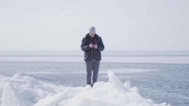 Sıcak kış ceket gözlüklü yakışıklı sarı sakallı adam cep telefonu fotoğraf çekerken buzulda buz bloğu üzerinde ayakta. Kış aylarında turist seyahatleri