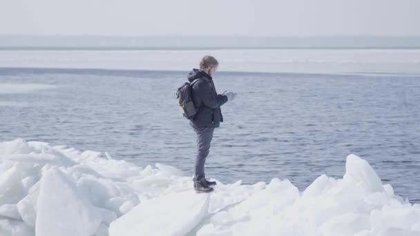 自信的男人穿着暖和的外套站在冰川上,拉直头发,望向远方。雪湖和冰川的神奇自然。站在冰上的人 — 图库视频影像