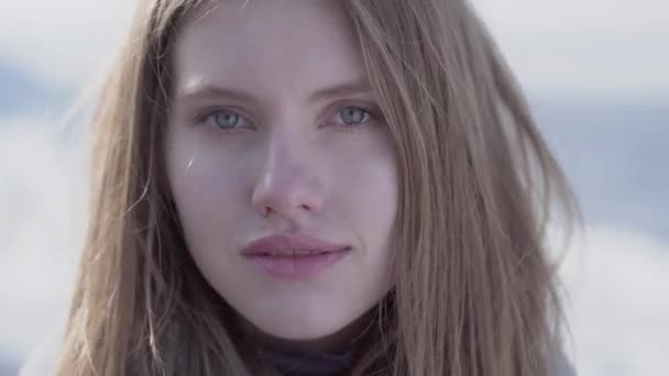 Close-up portrait of beautiful young blond woman with long hair and blue eyes looking in the camera. Attractive woman of Scandinavian appearance on glacier — Stock Video