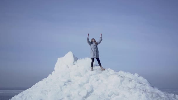 Blonde vrouw met lang haar in warme vacht staande op de top van de gletsjer het gooien van haar handen, triomcheren. Prachtig uitzicht op een besneeuwde Noord-of Zuidpool. De dame op het ijsblok — Stockvideo