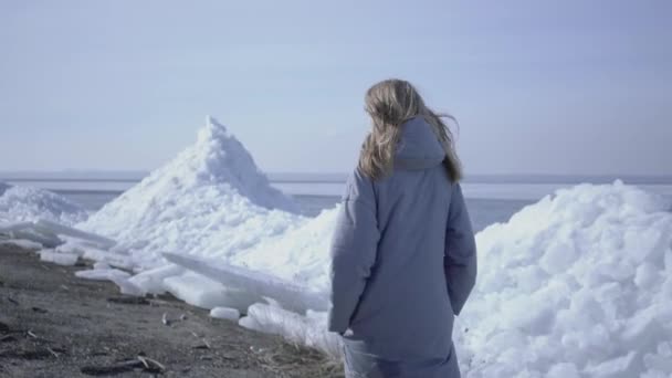 暖かいジャケットを着た若い女性が氷河を歩いている。雪の北極や南極の素晴らしい性質。氷のブロックの勇敢な女性極探検家. — ストック動画