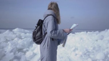 Sırt çantası ile çekici sarışın kadın Kuzey veya Güney Kutbu buz önünde Haritayı kontrol. Kışın turist seyahatleri. Kız kaybolur ve bir yol bulmak istiyor