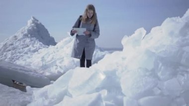 Elleri harita ile buzul üzerinde yürürken sıcak ceket kayma genç üzgün sarışın güzel kadın. Karlı Kuzey veya Güney Kutbu inanılmaz doğası. Buz blokları ile çevrili turist. Bayan kayıp