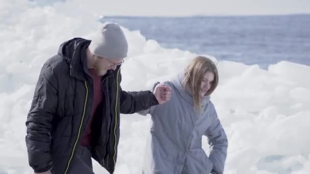 Csinos szakállas férfi séta aranyos nő kezében, a srác segít a barátnője mászni a jégtömbök.. Gyönyörű kilátás a havas északi vagy déli pólus. Néhány turista a gleccseren — Stock videók