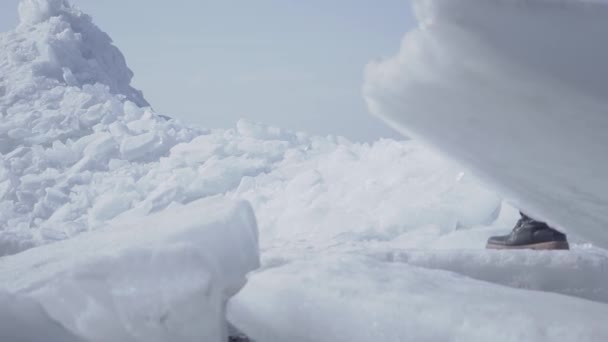 氷河の頂上を登る背景に男性観光客。雪の北極または南極の素晴らしい眺め。前景の氷塊がクローズアップされます。冷たい美しさ — ストック動画
