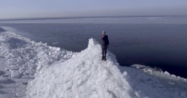 Kış Denizi sahilinin yakınında buz buzulları üzerinde kalan genç aktif mutlu adamın hava dron görünümü. Drone bir adamın eline uçuyor..