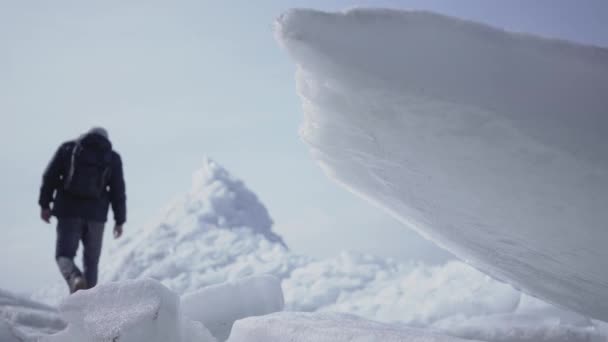 Ο αρσενικός τουρίστας στο παρασκήνιο ανεβαίνει στην κορυφή του παγετώνα. Υπέροχη θέα από ένα χιονισμένο Βορρά ή νότιο πόλο. Οι πάγοι στο μπροστινό πλάνο κλείνουν. Κρύα ομορφιά — Αρχείο Βίντεο
