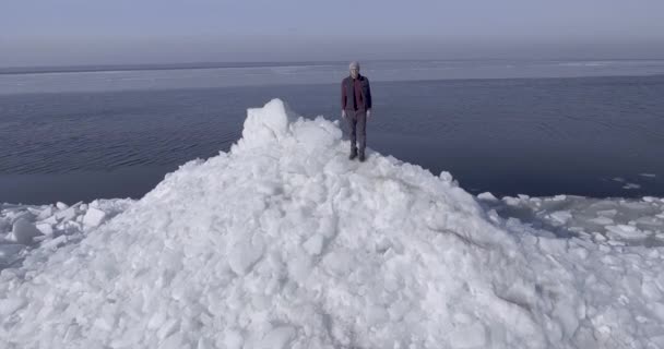 Vista aérea del dron del joven hombre feliz activo que permanece en los glaciares de hielo cerca de la costa del mar de invierno. Vista del dron . — Vídeo de stock