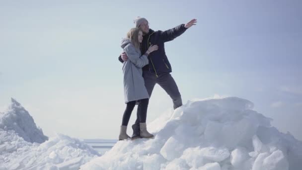 Schönes blondes Paar, das wegzeigt und sich umarmt. der bärtige Mann mit Brille und die attraktive Frau, die im Winter die Natur bewundert. Touristen reisen gemeinsam — Stockvideo