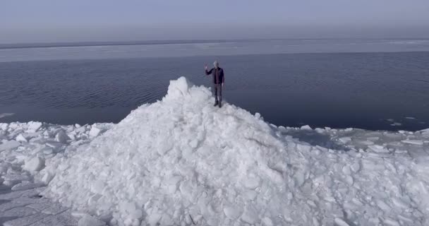 Vista aérea del dron del joven hombre feliz activo que permanece en los glaciares de hielo cerca de la costa del mar de invierno estrechando la mano. Vista del dron — Vídeo de stock