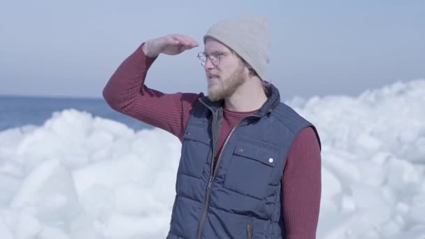 Ung stilig man turist fokuserade på något i närheten av kall is snöar glaciär bakom vinter havet. Slow motion — Stockvideo