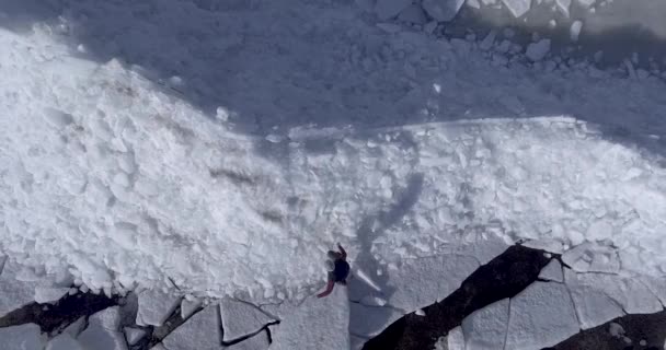 Vista aérea del dron del joven hombre feliz activo caminando sobre los glaciares de hielo cerca de la costa del mar de invierno. Vista del dron . — Vídeo de stock