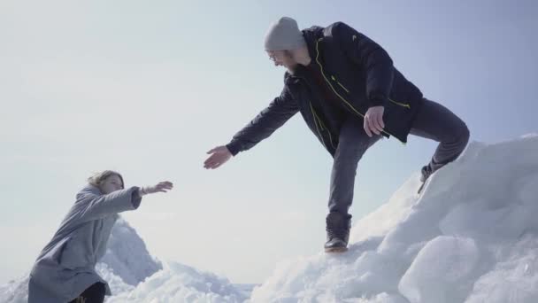 英俊的金发男子伸出手有吸引力的年轻女子帮助她爬上冰块。一对游客正在探索冰川。人们拥抱 — 图库视频影像