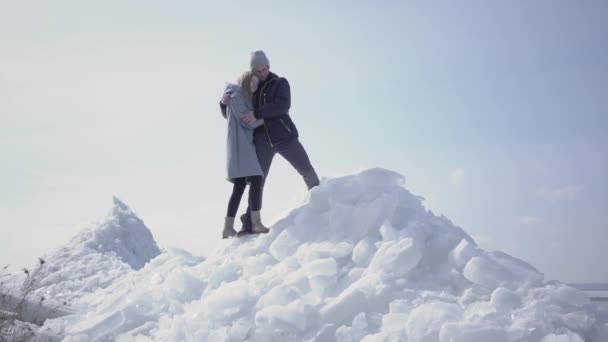 Hermosa pareja rubia apuntando lejos abrazándose. El hombre barbudo en las gafas y la mujer atractiva que admira la naturaleza en invierno. Los turistas viajan juntos — Vídeos de Stock