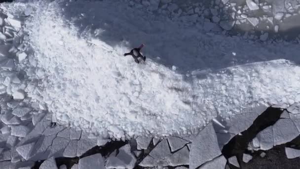 겨울 바다의 해안선 근처 얼음 빙하에 머물고 젊은 활동적인 행복한 남자의 공중 드론보기. 맨 위 보기 — 비디오