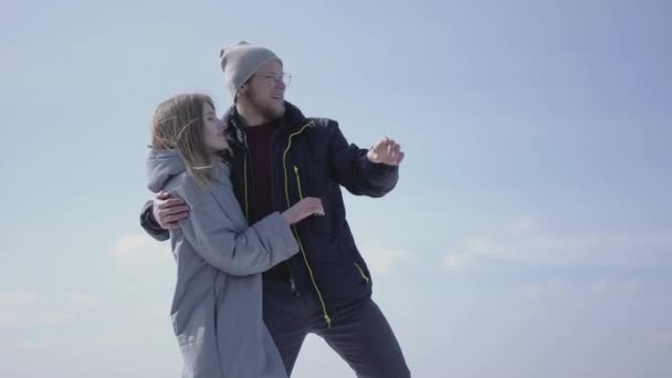 Beau couple blond pointant du doigt s'embrassant. L'homme barbu dans des lunettes et femme attirante admirant la nature en hiver. Les touristes voyagent ensemble — Video