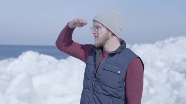 Der junge, gut aussehende Geologe konzentrierte sich auf etwas in der Nähe des kalten, schneebedeckten Gletschers hinter dem winterlichen Meer. Zeitlupe — Stockvideo