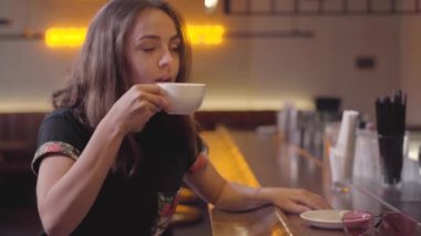 Bar tezgahında oturan kahvesinin tadını çıkaran çekici genç kadının portresi. Güzel kız modern kafe veya barda rahatlatıcı. Kahve molası