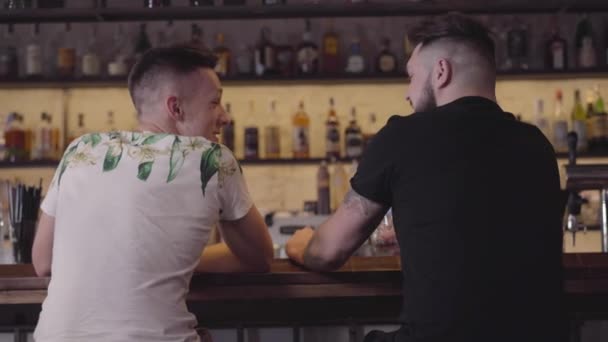 Twee mannen zitten aan de bar tegen het drinken van Elite alcohol. Jongens Clink bril en keer kijken naar de camera. Dag uit. — Stockvideo