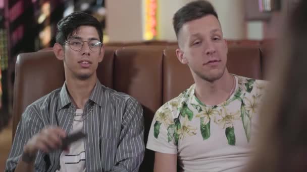 Retrato de dos amigos sentados en el sofá de cuero hablando con la chica en el restaurante. Feliz compañía joven descansando en un cómodo café — Vídeos de Stock