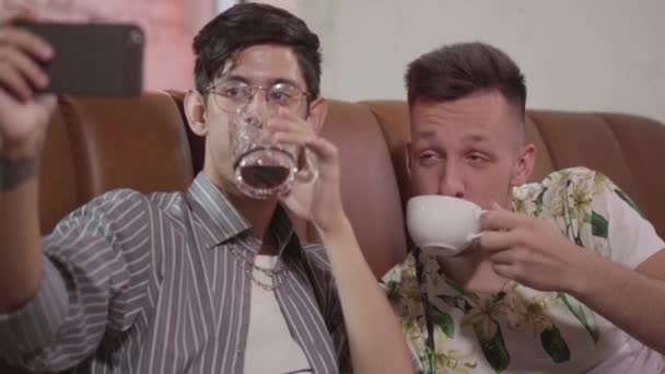 레스토랑에서 쉬고 있는 두 남자 친구의 초상화가 핸드폰으로 셀카를 찍고 있다. 한 남자가 술을 마시고, 또 다른 커피를 마셨다. 건강하고 건강에 해로운 라이프 스타일의 개념. 메이트는 재미 — 비디오