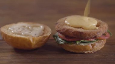 Burger yakın çekim yapan şefin elleri. Pirişin üzerine eritilmiş peynir koyan aşçı, domates dilimleri ve fesleğen yaprakları bir hamburger topuzun un tek parçası üzerinde yatan. Lezzetli yemek hazırlama