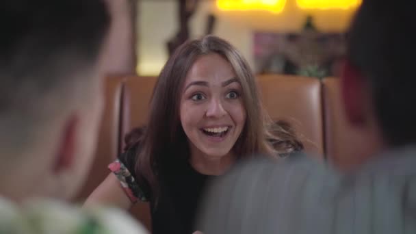 Jolie jeune femme émotionnelle assise dans le café confortable devant deux mecs riant de leur histoire. Étudiants insouciants s'amusant dans le restaurant. Loisirs intérieurs 