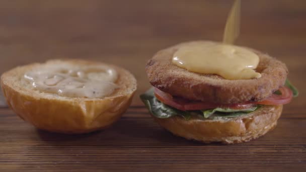 Hände des Kochs, der Burger aus nächster Nähe zubereitet. Der Koch legt geschmolzenen Käse auf das Schnitzel, Tomatenscheiben und Basilikumblätter, die auf einem Stück eines Hamburgerbrötchens liegen. Leckere Speisenzubereitung — Stockvideo