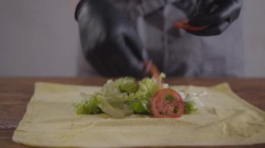 Shawarma yakın çekim yapma siyah mutfak eldivenleri şefin elleri. Pideye domates ve soğan koyarak aşçı. Lezzetli arap çerez hazırlama