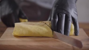 Shawarma yakın çekim yapma siyah mutfak eldivenleri şefin elleri. Aşçı kesme iki parça üzerinde shaurma haddelenmiş ve ahşap tahta üzerine koyarak. Lezzetli arap çerez hazırlama