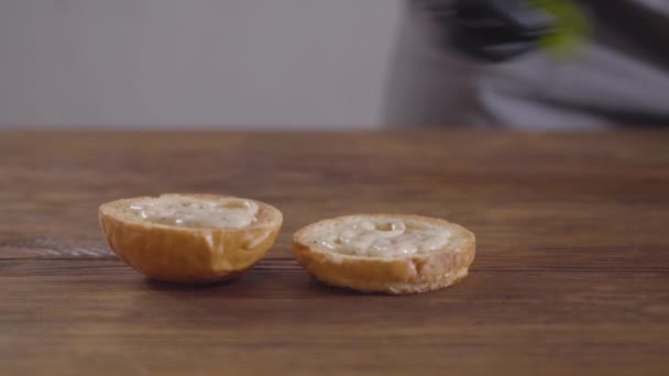 Mains du chef en gants de cuisine noirs pour faire un gros plan du hamburger. Le cuisinier mettre des feuilles de basilic sur le morceau d'un pain de hamburger. Préparation des aliments savoureux — Video