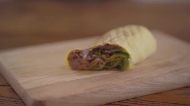 Tangan dari koki dalam sarung tangan dapur hitam membuat shawarma close-up. Tukang masak meletakkan setengah shawarma dengan saus di atasnya di papan kayu. Makanan ringan arab lezat yang disajikan — Stok Video