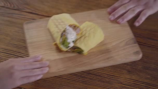 Shawarma savoureux avec de la sauce couché sur la planche en bois. Des mains masculines et féminines qui mangent. L'homme et la femme partagent le shaurma. Savoureux service de collation arabe. Vue du dessus — Video